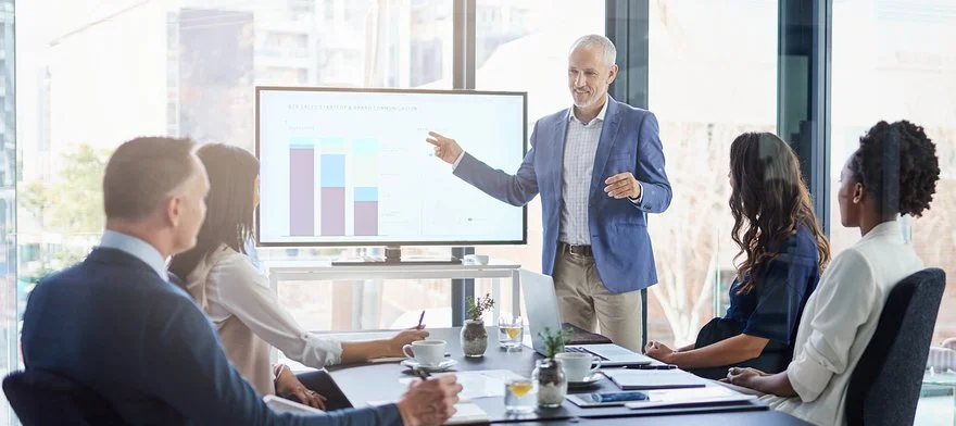 Presenter addressing a meeting room in front of a chart display