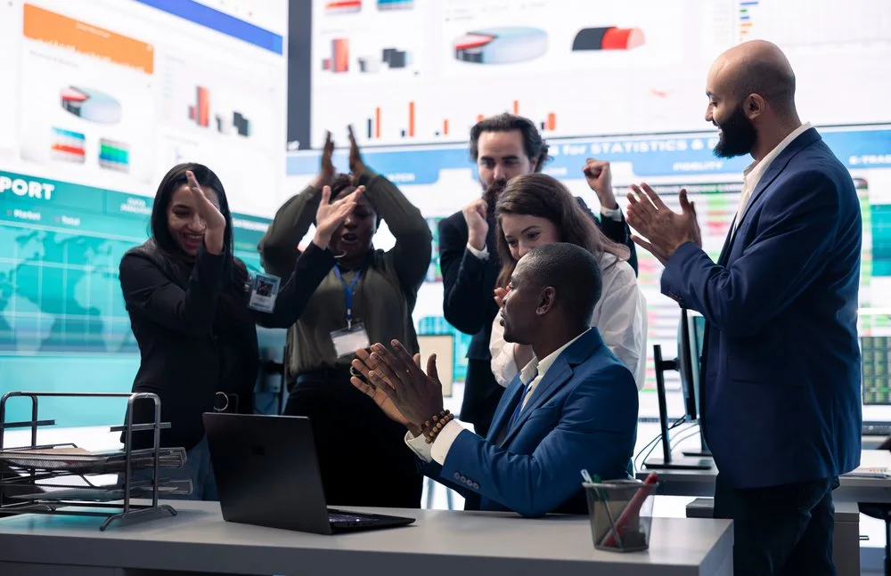 Colleagues applauding in front of a trading screen wall
